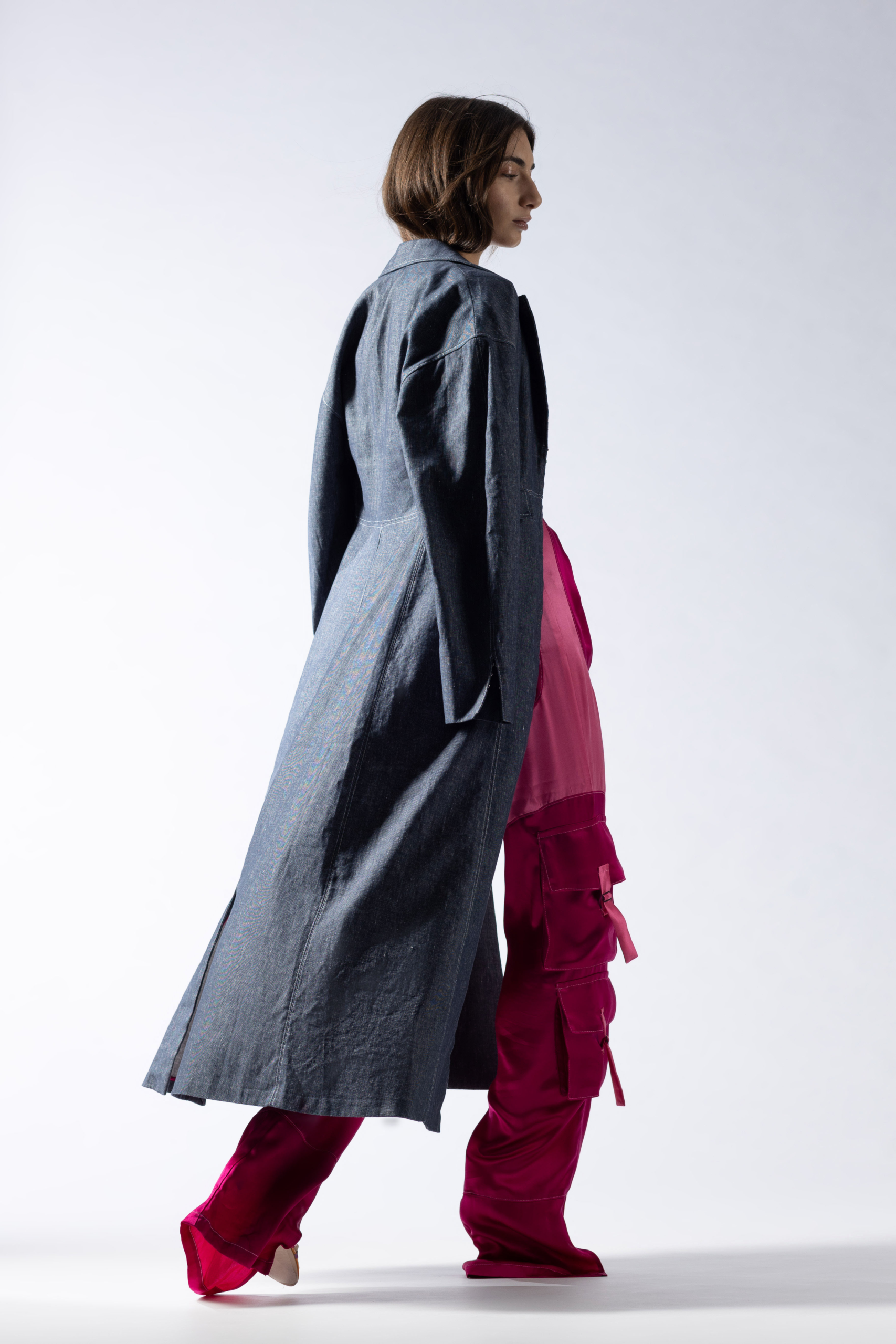 high end fashion studio editorial of model from behind, full body, with pink cargo trousers and jeans trenchcoat
